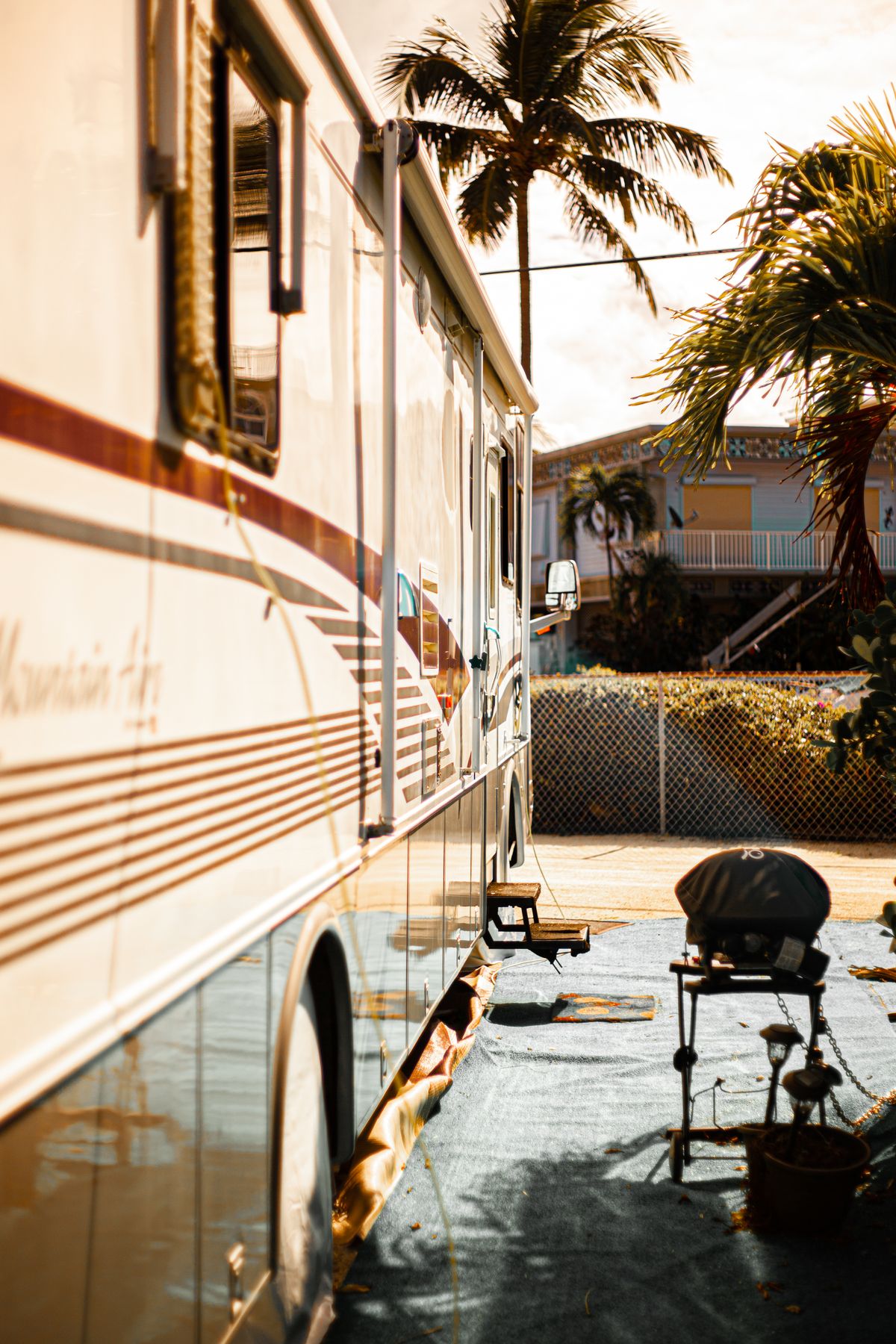 Harsh afternoon sun beating on the appliance-vent side of a motorhome parked at an RV site with palm trees