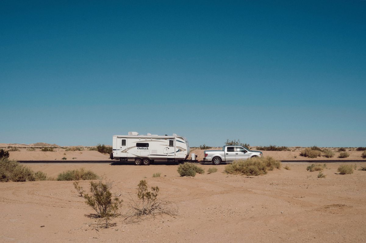 Truck towing a travel trailer through open Sonoran desert scrub under a deep blue sky